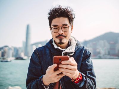年轻的亚洲男子在散步时愉快地使用智能手机