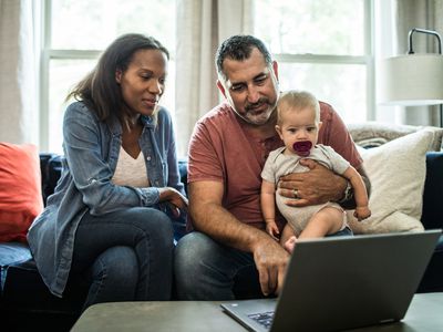 丈夫和妻子抱着婴儿，看笔记本电脑