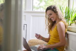 输入信用卡信息的微笑的妇女在膝上型计算机“width=