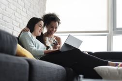 快乐的女同性恋夫妇坐在家里的沙发上网购的低角度视图。