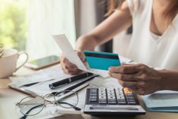 女人在办公桌前用计算器用信用卡支付她每月的账单